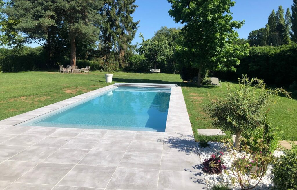 Piscine Aquinox sur mesure avec bassin rectangulaire, terrasse carrelée et jardin paysager